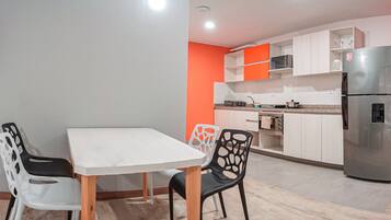 A modern kitchen with white cabinets, a stainless steel refrigerator, and a dining area with a white table and black chairs.