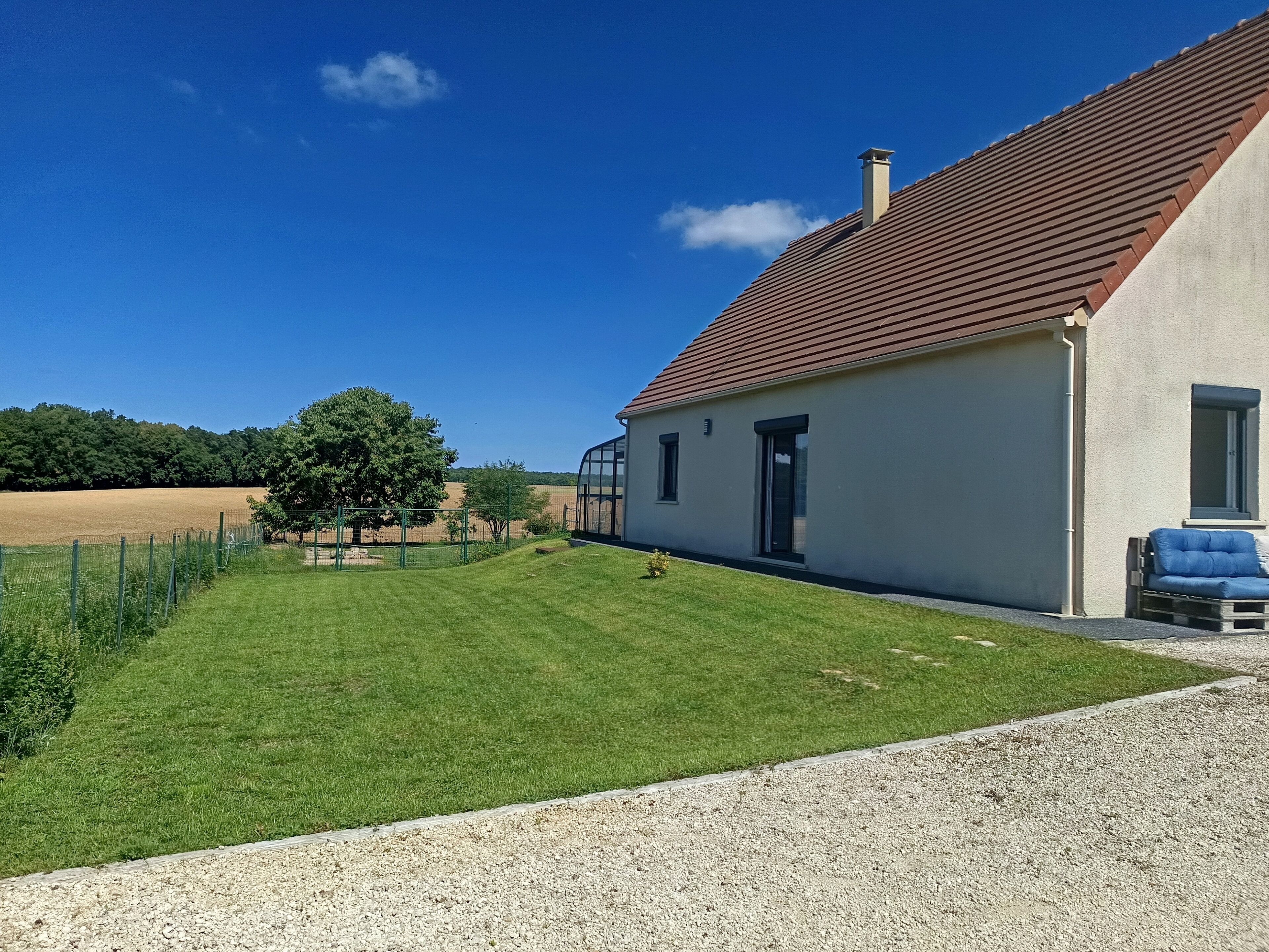 A house with a red-tiled roof, a small garden, and a clear blue sky.