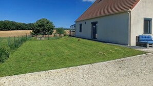 A house with a red-tiled roof, a small garden, and a clear blue sky.