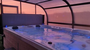 A hot tub with a canopy, surrounded by a wooden deck, and a view of a sunset through the canopy.