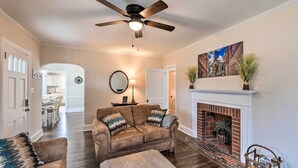 A living room with a fireplace, a ceiling fan, and a dining area in the background. - New Bern Retreat w/ Fire Pit ~ 1 Mi to Dtwn! (New Bern)