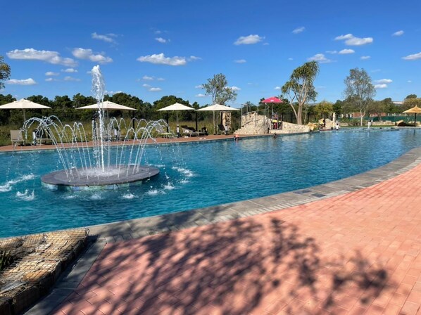 Relax by the serene pool, surrounded by trees and umbrellas, and enjoy the soothing sound of the central fountain.