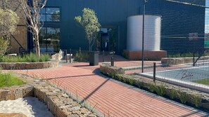 Stroll along the paved walkway to the entrance of this modern building, surrounded by lush greenery and a secure metal fence.