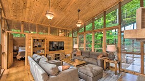Una cabaña espaciosa con un televisor grande, asientos cómodos y ventanas amplias que dan a un bosque.