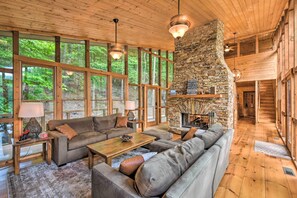 Un salón espacioso con chimenea de piedra, ventanas amplias y piso de madera.