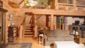 Interno di una baita in legno con una scala in legno, un divano, un tavolino e una zona cucina.