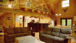 Un'ampia zona giorno con soffitto alto e travi in legno, una sala da pranzo con tavolo e sedie, e una cucina sullo sfondo.