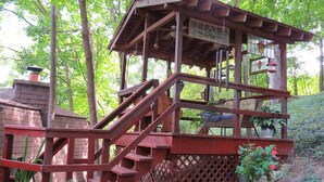 A wooden deck with a staircase leading to a covered area with a window and a hanging light fixture.