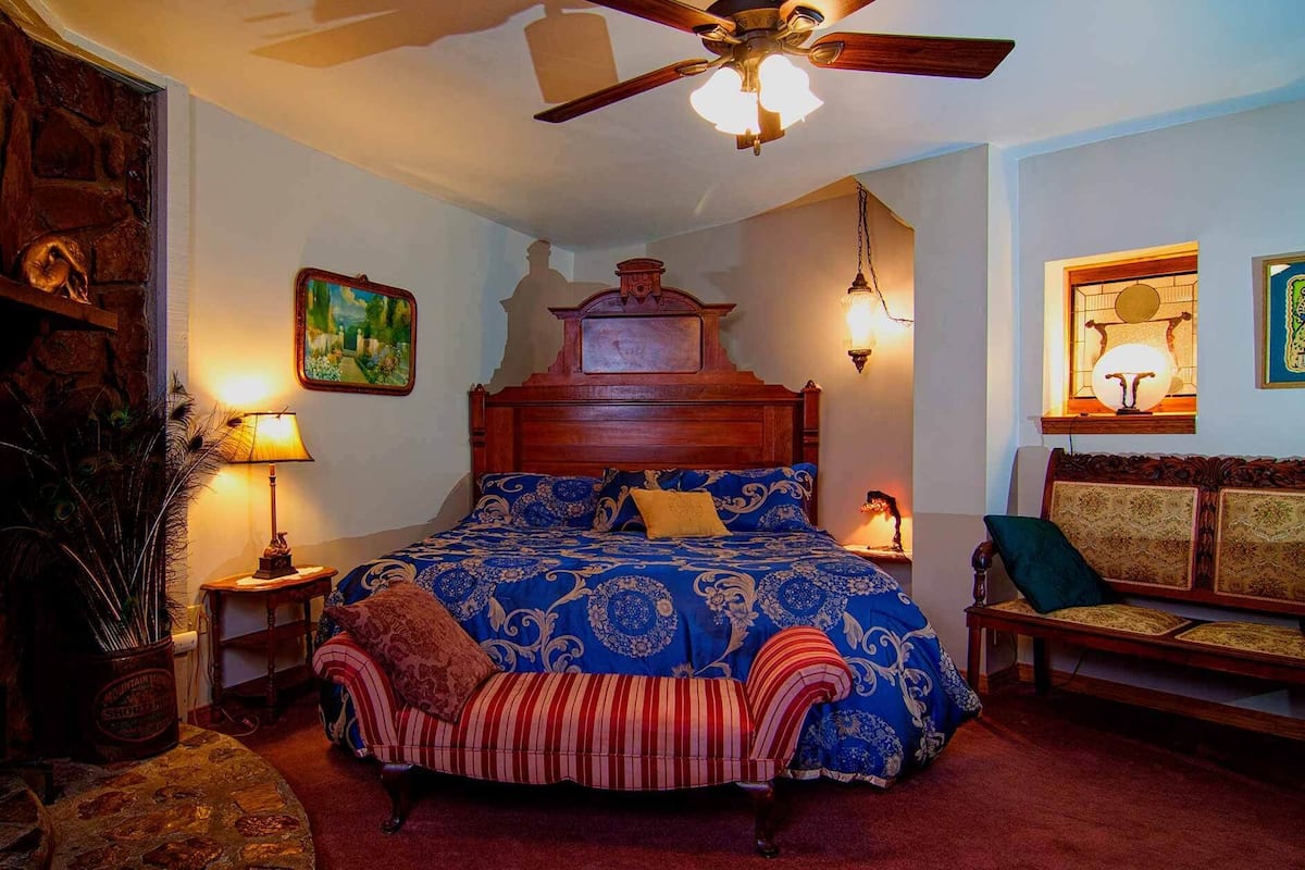 A bedroom with a large bed, a wooden headboard, a ceiling fan, and a bench with a cushion.