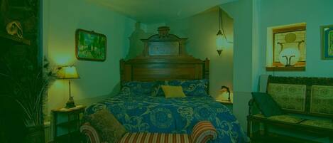 Une chambre à coucher avec un grand lit, une tête de lit en bois, une table de chevet avec une lampe, un banc avec un coussin et une étagère murale agrémentée d’un objet décoratif.