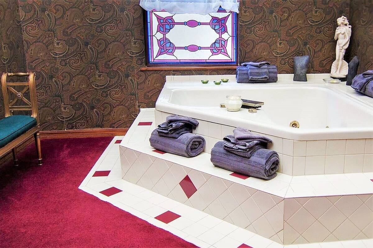 A bathroom with a bathtub, a wooden chair, a red carpet, and a decorative wall.