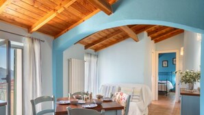Un'area pranzo con soffitto in legno, un tavolo apparecchiato per quattro persone e vista su una camera da letto sullo sfondo.