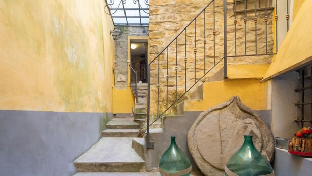 Una stretta scala con parete in pietra e ringhiera in metallo, che conduce a un piano superiore.