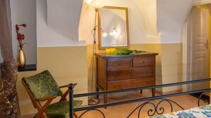 A bedroom with a wooden dresser, a green chair, a mirror, and a vase with flowers. - Apartment Giallo by Interhome (Vasia)