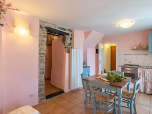 A cozy kitchen with a stone wall, a dining area with blue chairs, and a small table with a plant.
