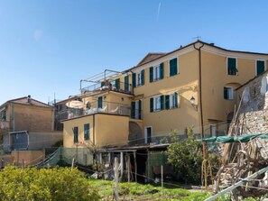 A multi-story yellow building with green shutters, balconies, and a stone wall.
