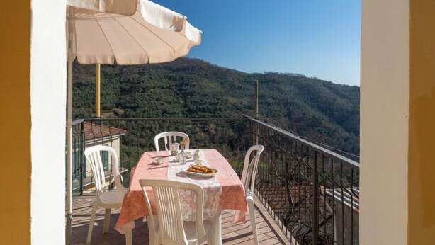 An outdoor dining area with a table and chairs, a large umbrella, and a scenic mountain view.