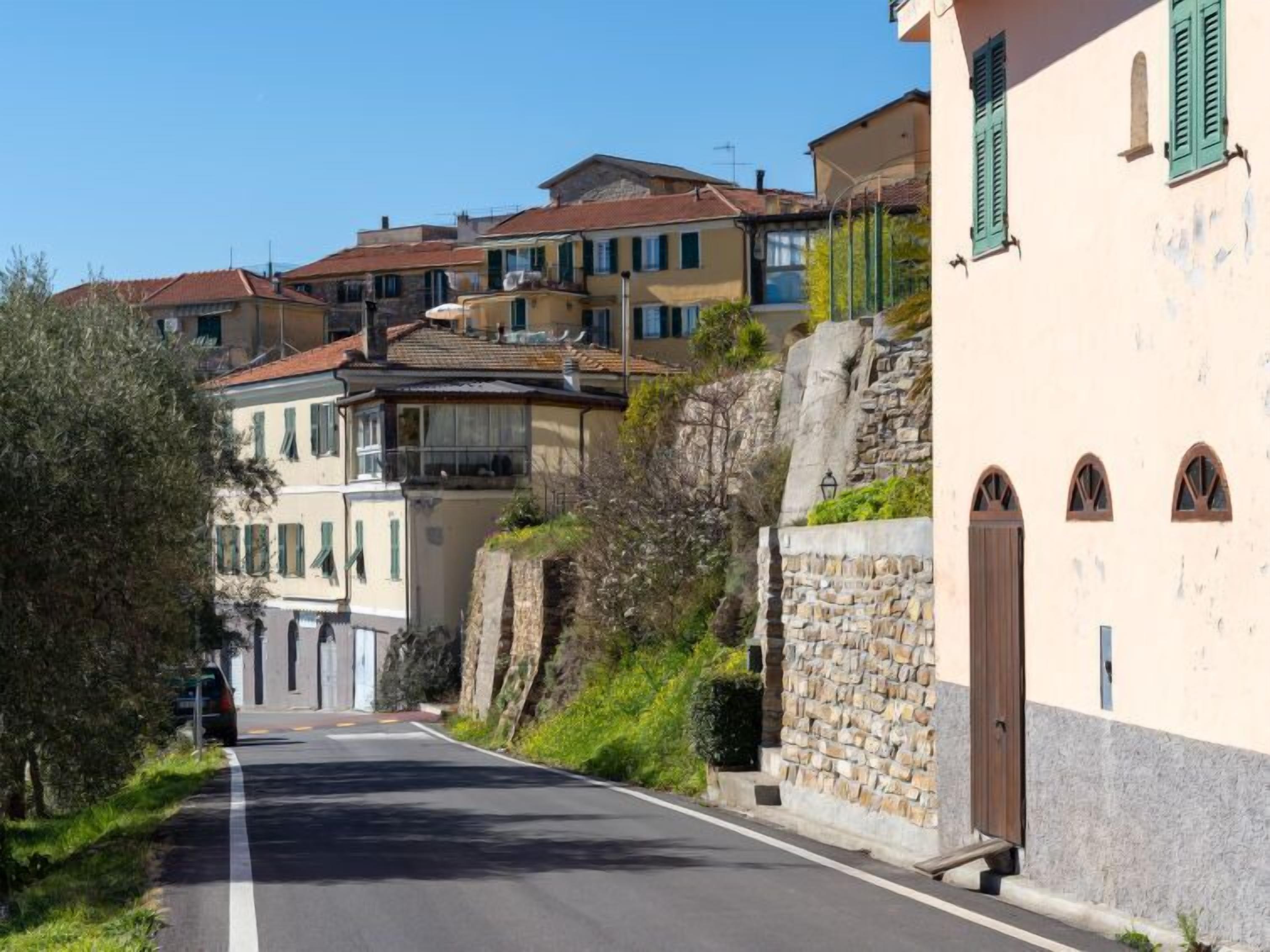 A narrow street flanked by traditional buildings with stone walls and wooden shutters, leading to a town center.