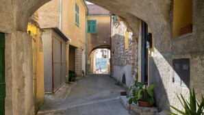 A narrow street with stone buildings, an archway, and a view of the countryside.