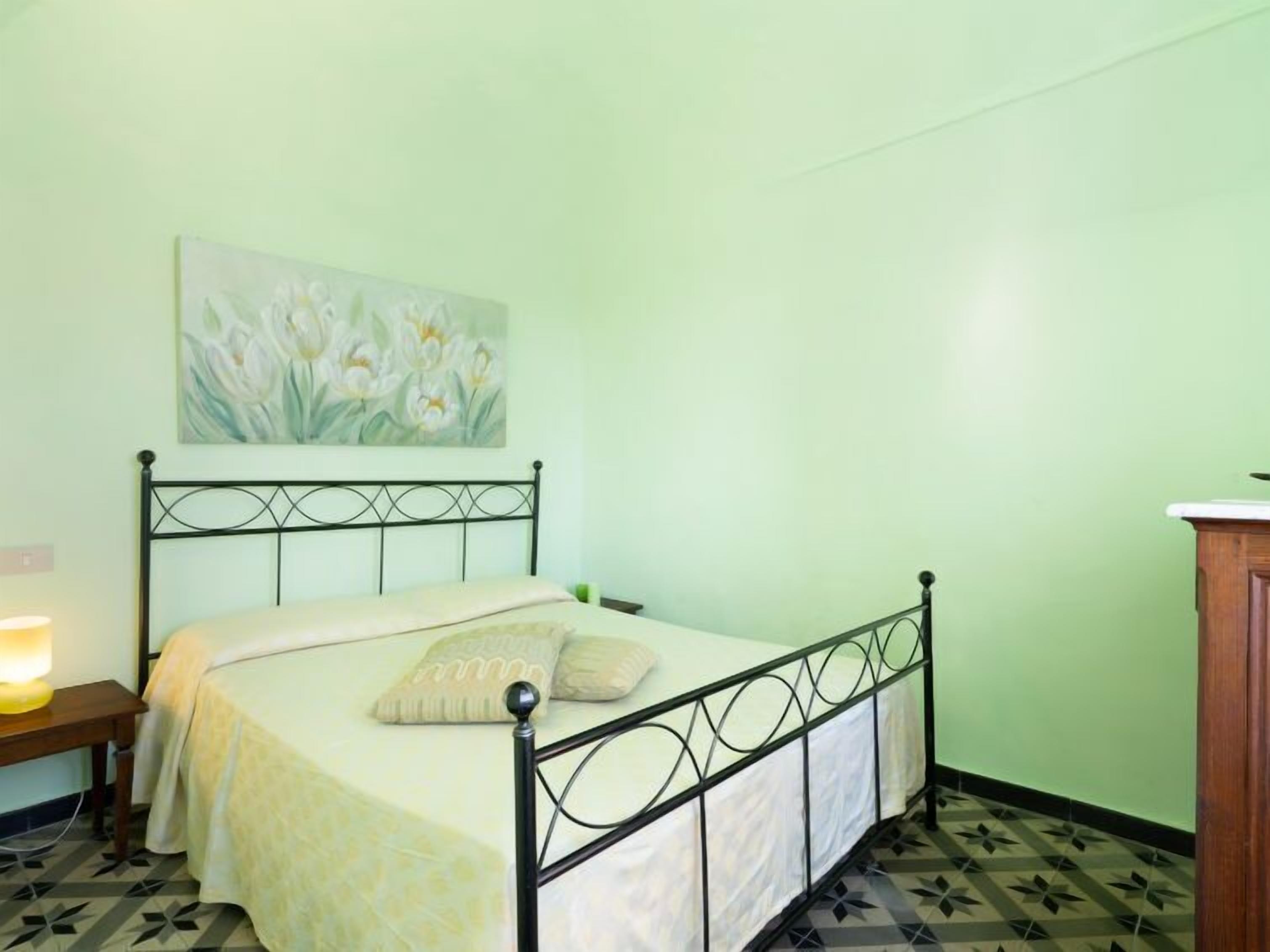 A single bed with a metal frame, a bedside table with a lamp, and a painting of flowers on the wall.