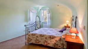 A bedroom with a bed, a nightstand, a lamp, and a window with curtains. - Apartment Verde by Interhome (Vasia)