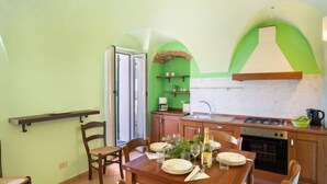 A compact kitchen with a dining area, featuring a wooden table set for four, a built-in oven, and a green accent wall. - Apartment Verde by Interhome (Vasia)