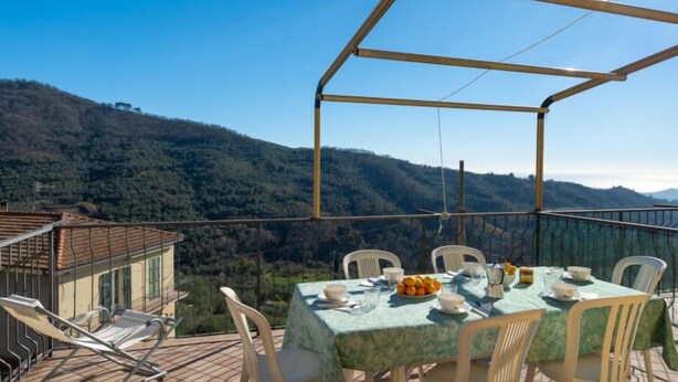 A terrace with a table set for dining, overlooking a mountainous landscape. - Apartment Verde by Interhome (Vasia)