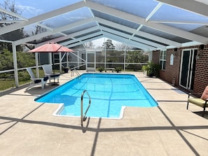 A covered outdoor swimming pool with a glass enclosure, a red umbrella, and a few lounge chairs.