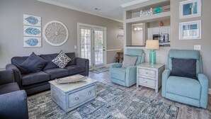 Una sala de estar con un sofá gris, sillones color turquesa, una mesa de centro y una cocina al fondo.