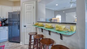 Una cocina con armarios blancos, un refrigerador de acero inoxidable, una encimera color aguamarina y cuatro taburetes de madera.