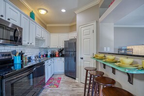 A modern kitchen with white cabinets, stainless steel appliances, and a teal backsplash.