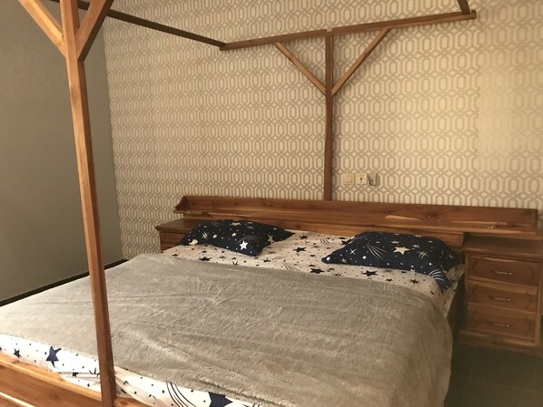 A bed with a canopy, a patterned wall, and a wooden nightstand.