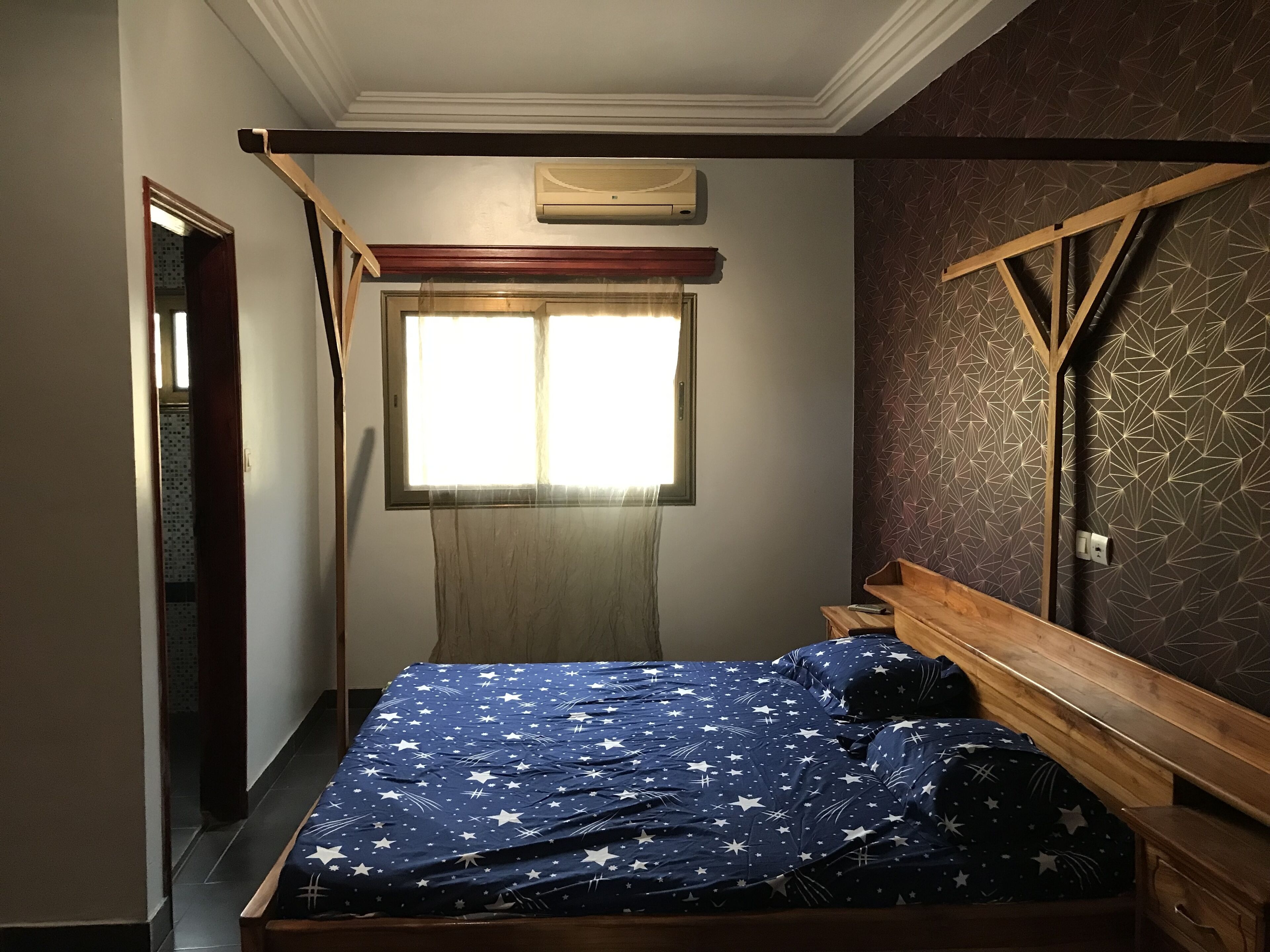 Une chambre à coucher avec un lit, une fenêtre et un mur décoré d’un motif.
