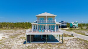 A two-story beachfront house with a balcony and a covered deck.