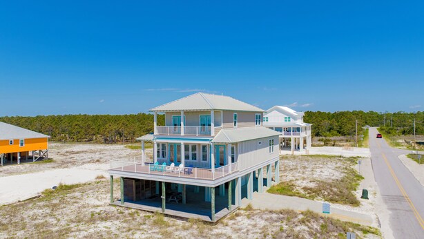 A two-story beachfront house with a balcony and a covered porch.