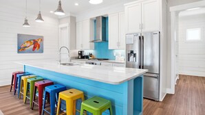 A modern kitchen with white cabinets, a blue island, and colorful stools.