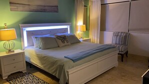 Un dormitorio ordenado con cama, lámparas de noche, una silla y un tapete estampado.