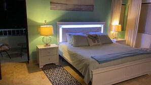 Un dormitorio con una cama, dos mesitas de noche, una lámpara, un tapete estampado y una ventana con cortinas.
