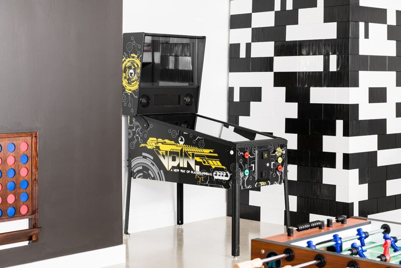 A room with a foosball table, a pinball machine, and a dartboard.