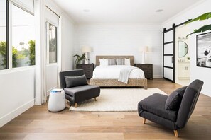 A modern bedroom with a large bed, a sitting area with a chair and ottoman, a side table, and a view of greenery outside. - Luxury Oasis~3.5mi from Scottsdale~Pool~Game Rm (Scottsdale)