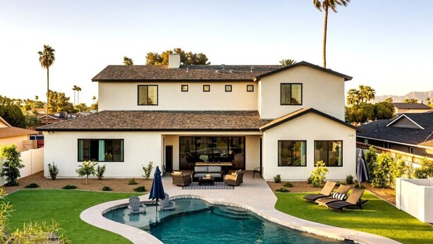 Una casa de dos pisos con piscina, mobiliario exterior y un césped bien cuidado.
