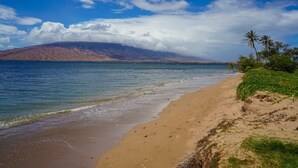 Ein Strand mit einem Berg im Hintergrund und blauem Himmel.
