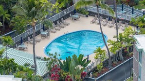 Une piscine entourée de chaises longues et de palmiers, avec un mur de pierre et un escalier menant à un niveau supérieur.