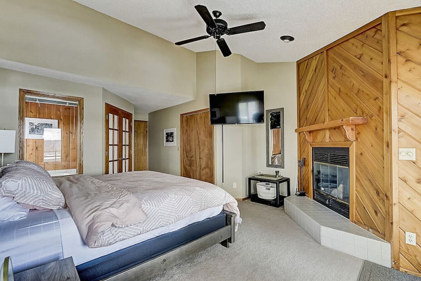 Een slaapkamer met een bed, een plafondventilator, een televisie, een open haard en houten wanden.