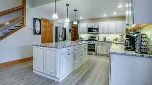 Cozinha moderna com armários brancos, bancadas de granito, eletrodomésticos de aço inoxidável e iluminação pendente.