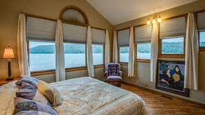Une chambre dotée d’un grand lit, d’une chaise et de plusieurs fenêtres donnant sur un lac.