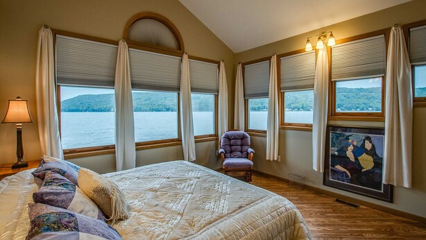Quarto com uma cama grande, uma cadeira e várias janelas com vista para um lago.