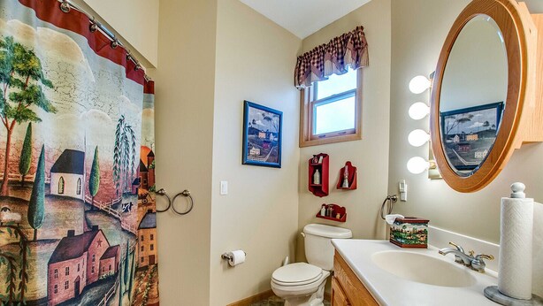 Une salle de bain avec une fresque murale, des toilettes, un lavabo avec un miroir et une fenêtre avec des rideaux.