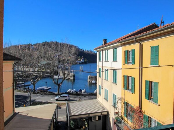 A yellow building with green shutters, a view of a lake with boats, and a tree in the foreground.