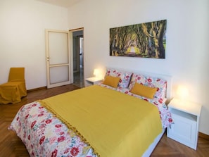 A bedroom with a bed, a chair, a painting, and a door.